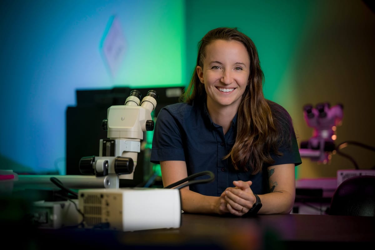 The author of this newsletter, Ashley Juavinett, sits at a table behind a microscope.